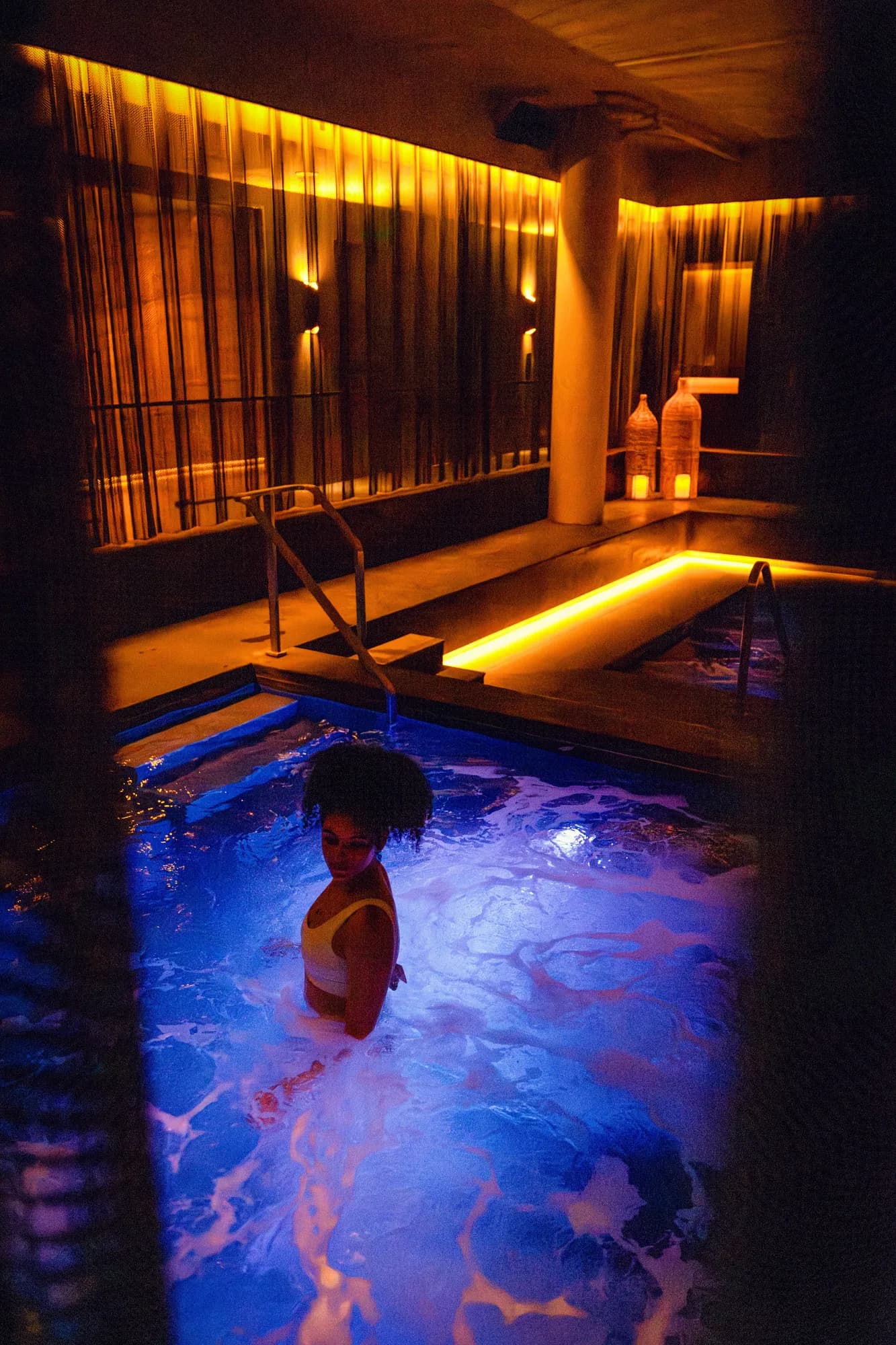 A guest soaking in the blue-lit Thermal Springs sanctuary